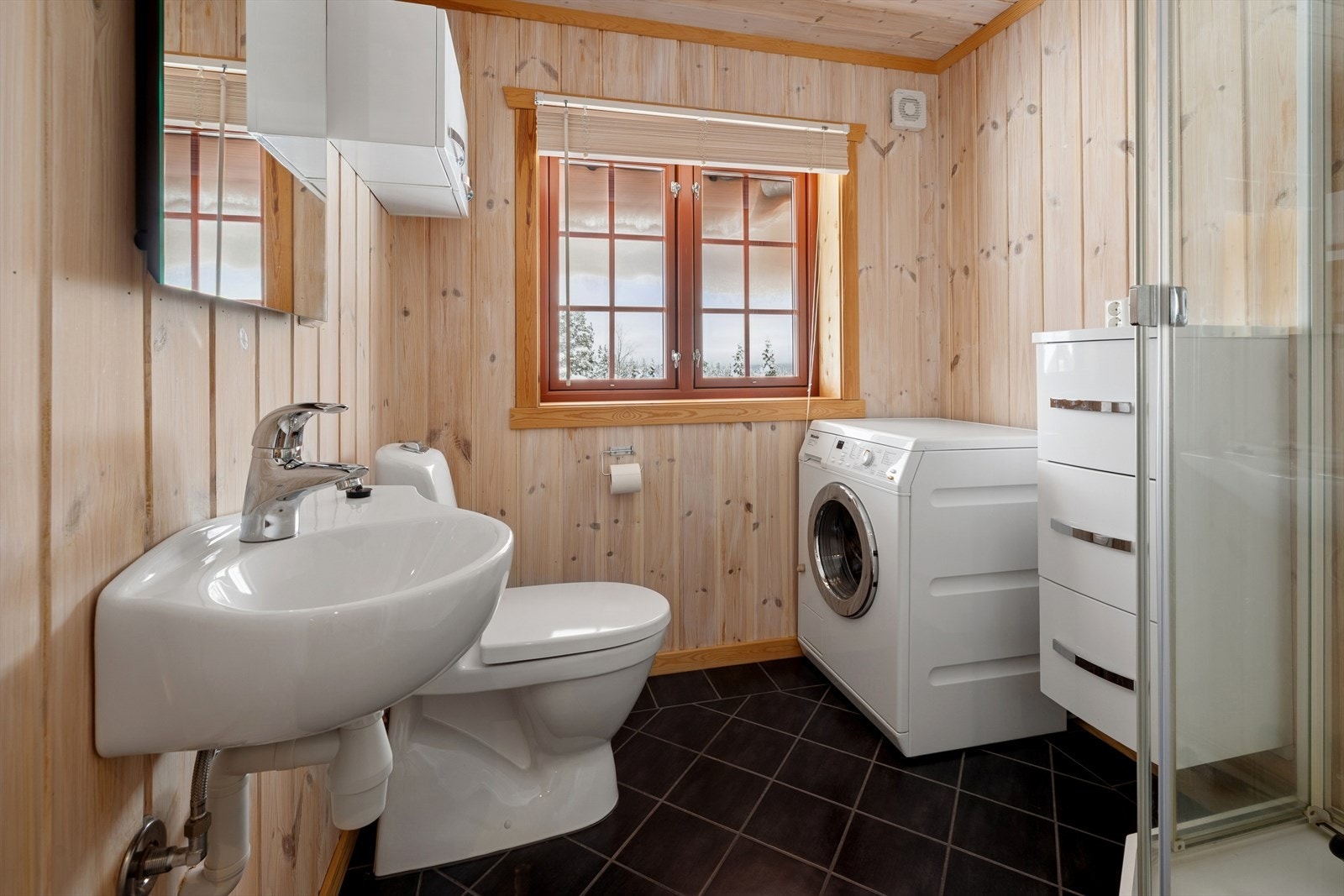 Badet har flislagt gulv med varmekabler. Det er innredet med dusjkabinett, toalett, baderomsinnredning og håndvask. Galleribilde