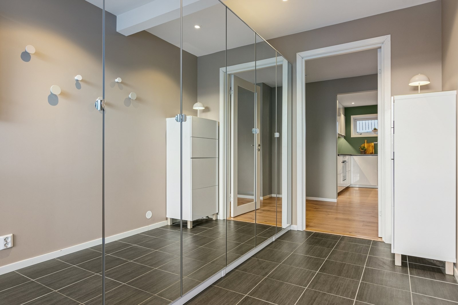 Inngangspartiet har flislagt gulv og en stor skyvedørsgarderobe med speilfronter. Galleribilde