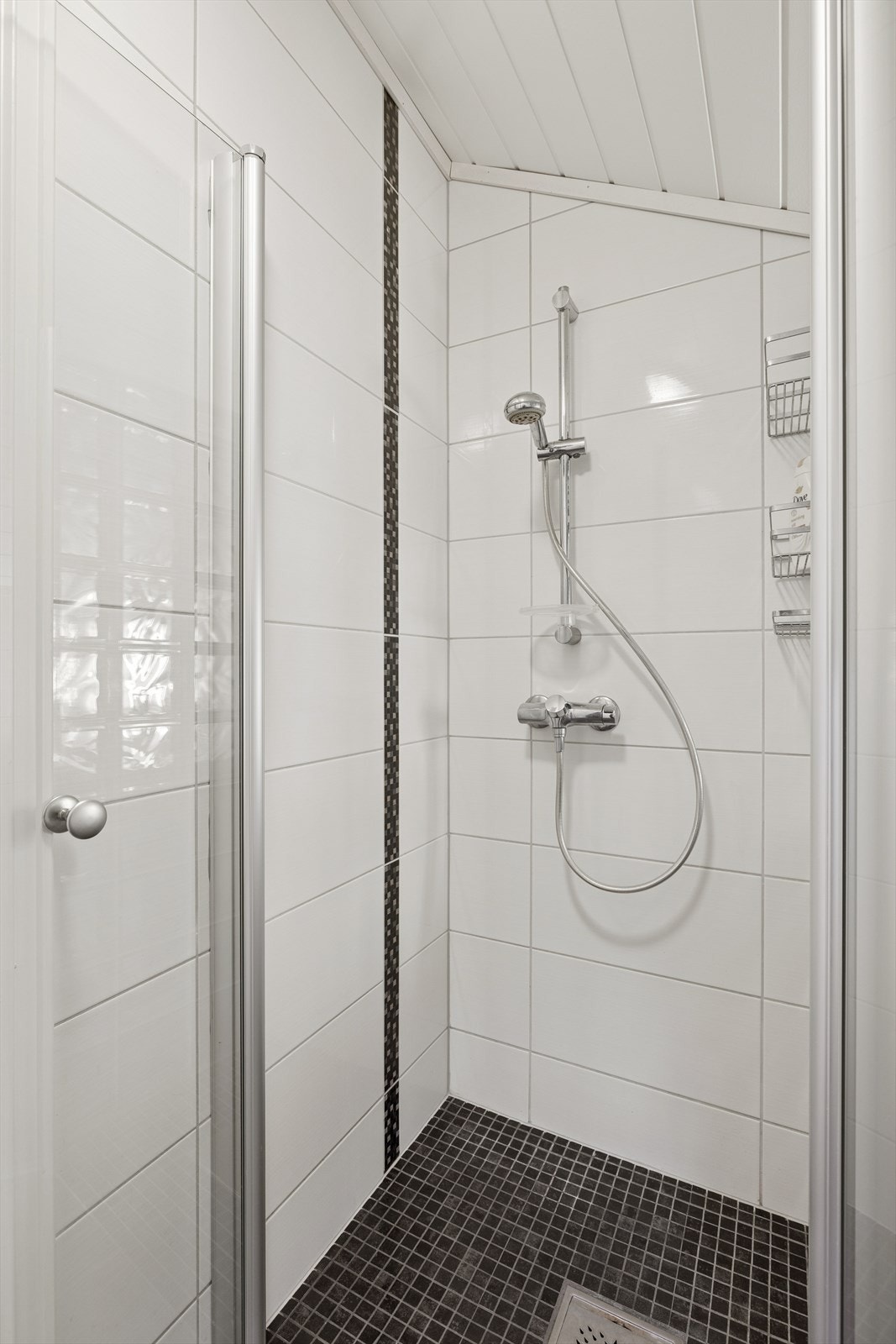 Badet er innredet med vegghengt toalett, dusj direkte på gulv med dusjdør, samt servantinnredning med underskap. Galleribilde