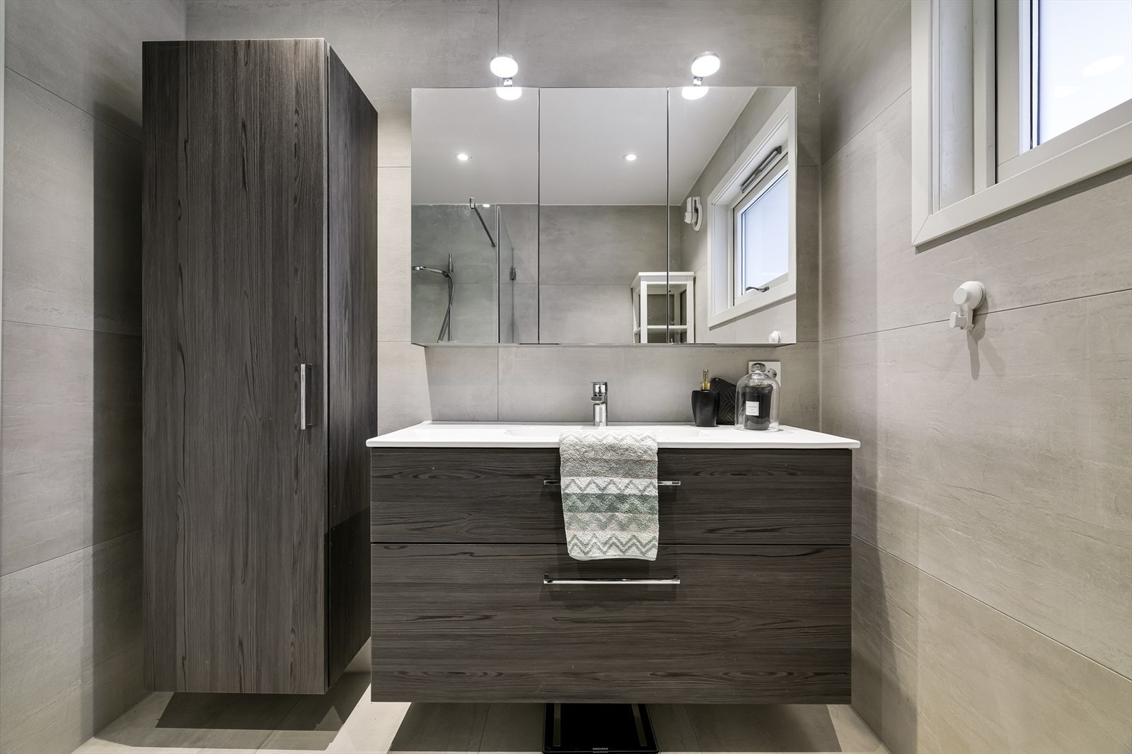 Badet har en moderne finish med store vegg- og gulvfliser i ulike grånyanser. Varme er lagt i gulvet Galleribilde