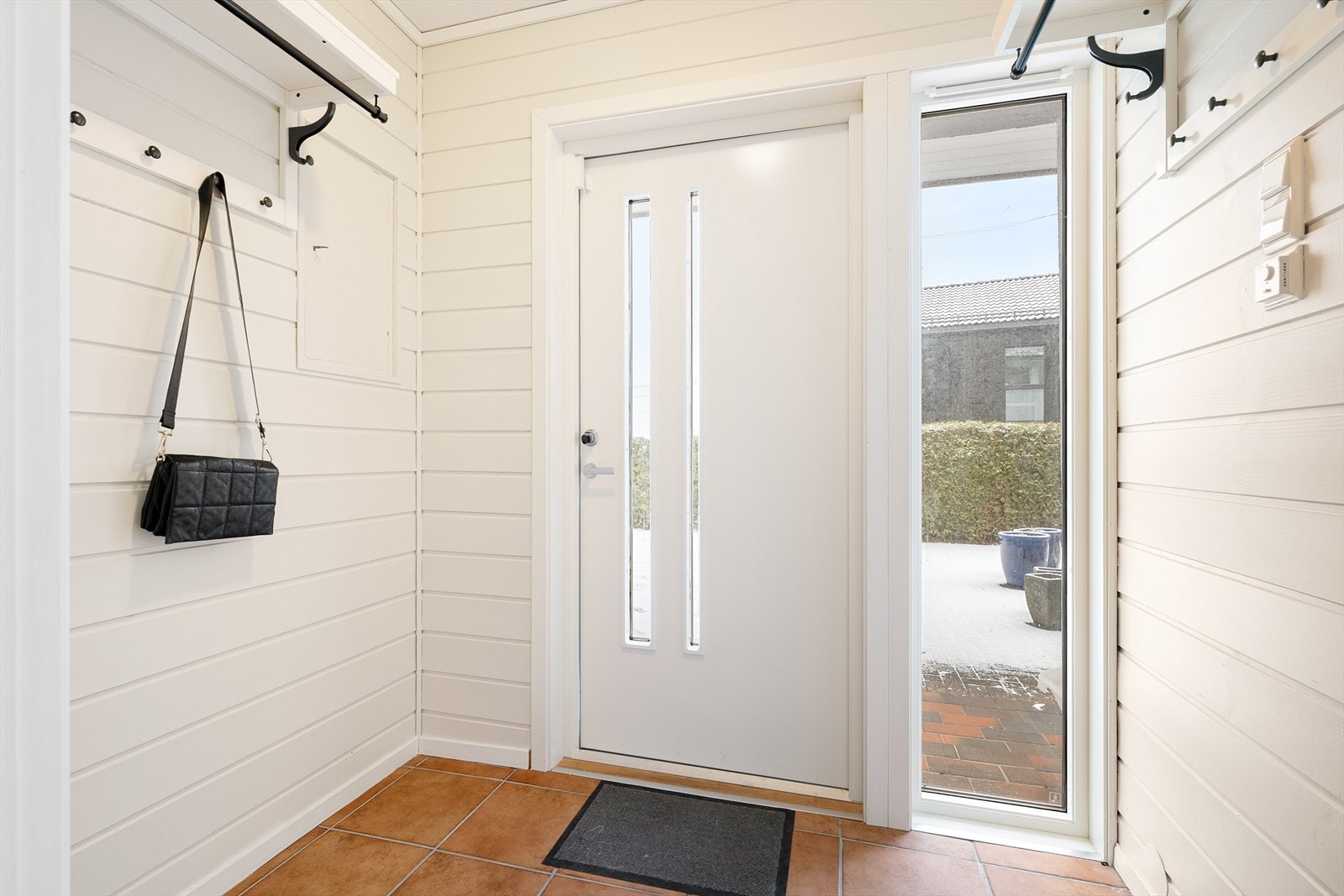 Vindfanget flislagt gulv og hvitmalte panelvegger, og her passer det fint å innrede med knagger og skohyller. Galleribilde