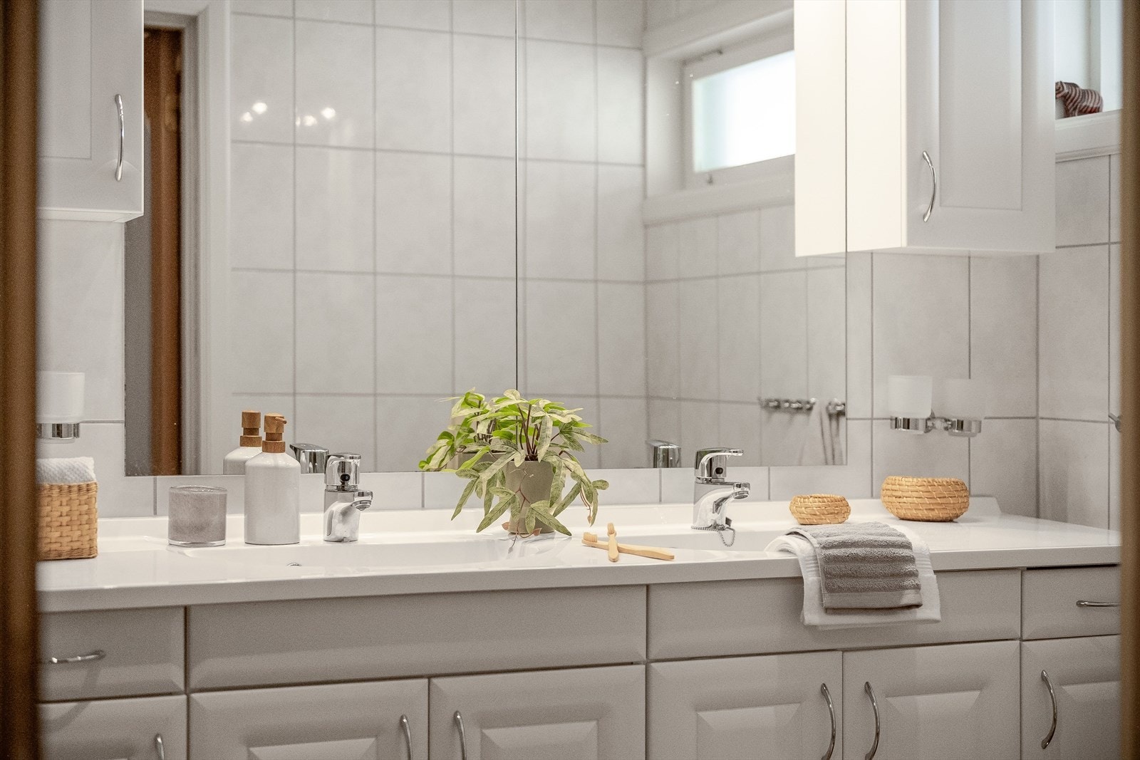 Lys og pen baderomsinnredning med profilerte fronter og heldekkende dobbel servant, vegghengte skap og stort speil med belysning over. Galleribilde