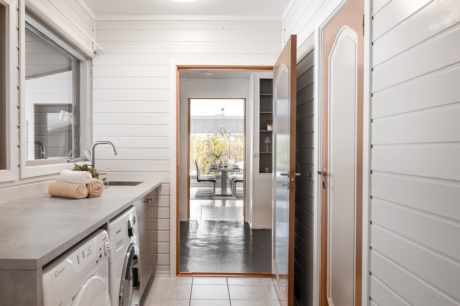 Fra kjøkkenet kommer du videre inn til et praktisk vaskerom med flislagt gulv og lysmalt panel på veggene. Galleribilde