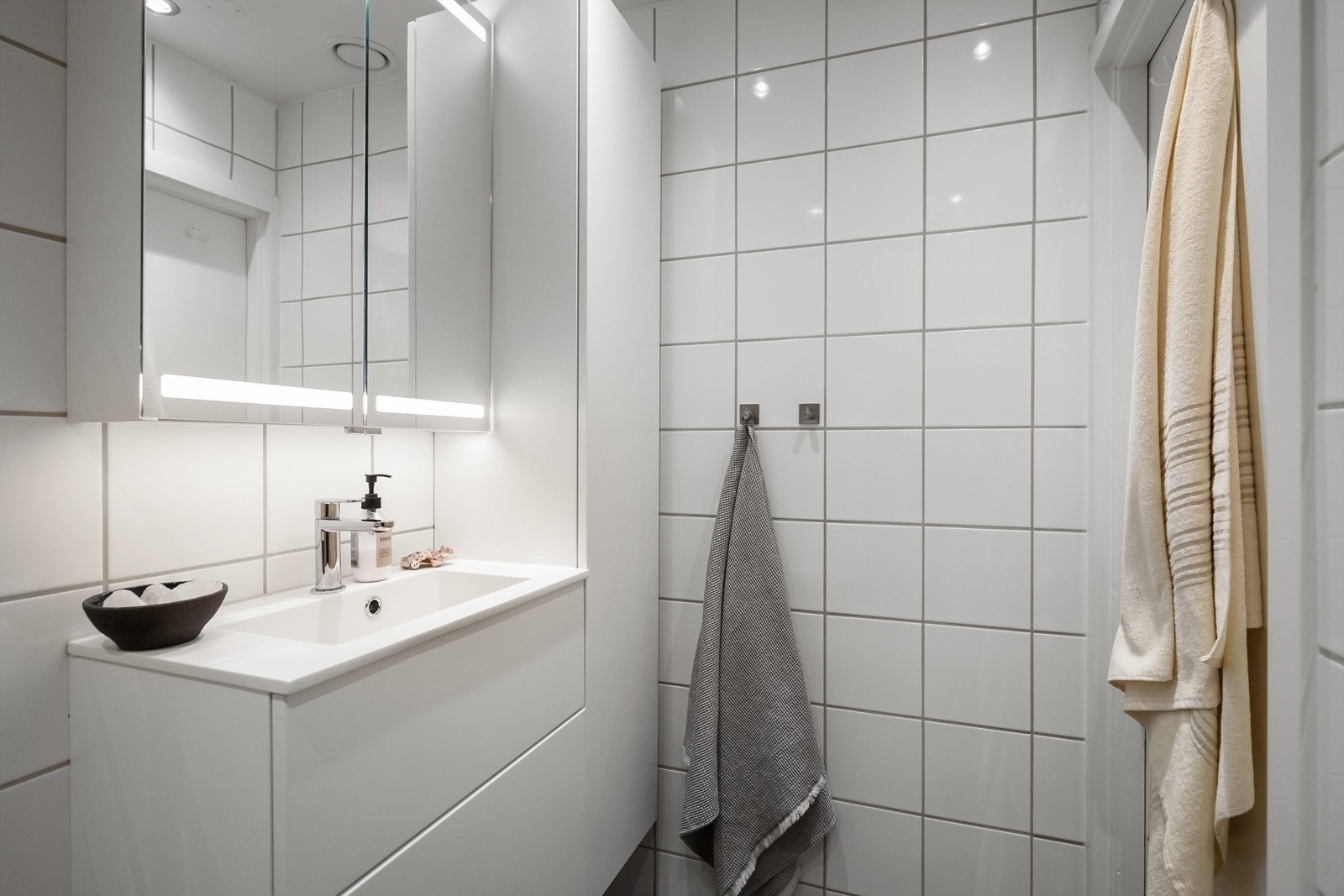 Videre er det en heldekkende servant med skuffeinnredning under, tilhørende skap på vegg og speilskap med integrert belysning Galleribilde