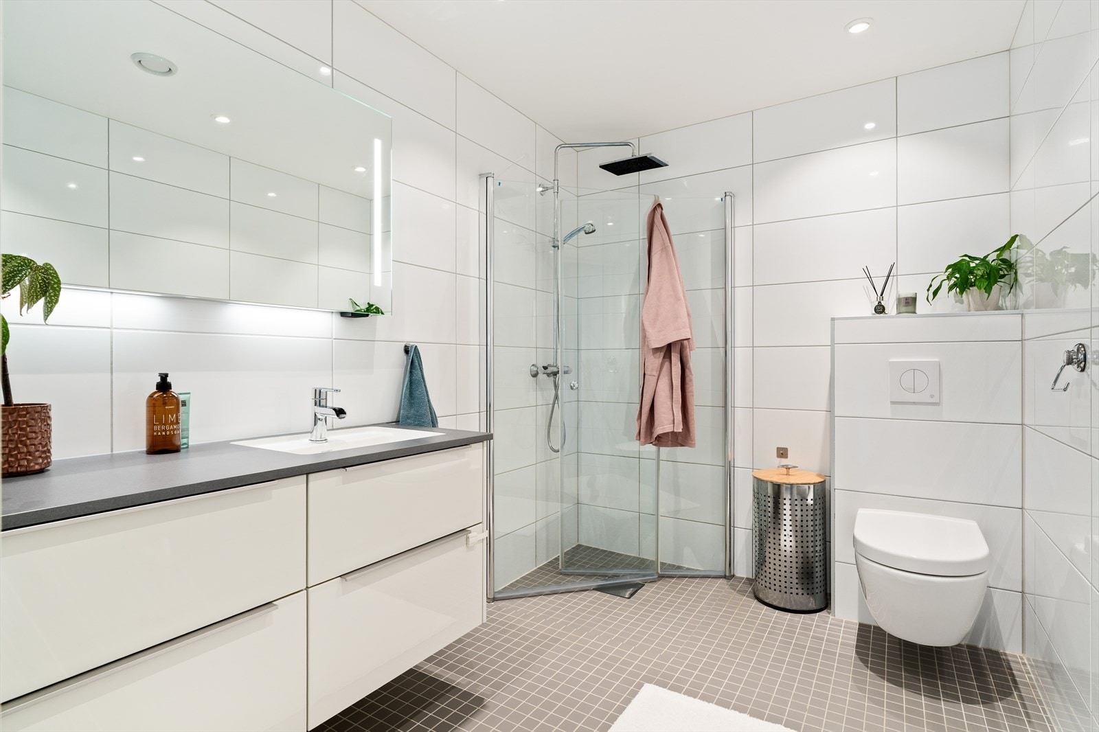 Badet er flislagt med behagelig gulvvarme og downlights i himling. Videre er badet utstyrt med en svært romslig innredning med servant, vegghengt toalett og dusjhjørne med innfellbare dører og regndusj. Galleribilde