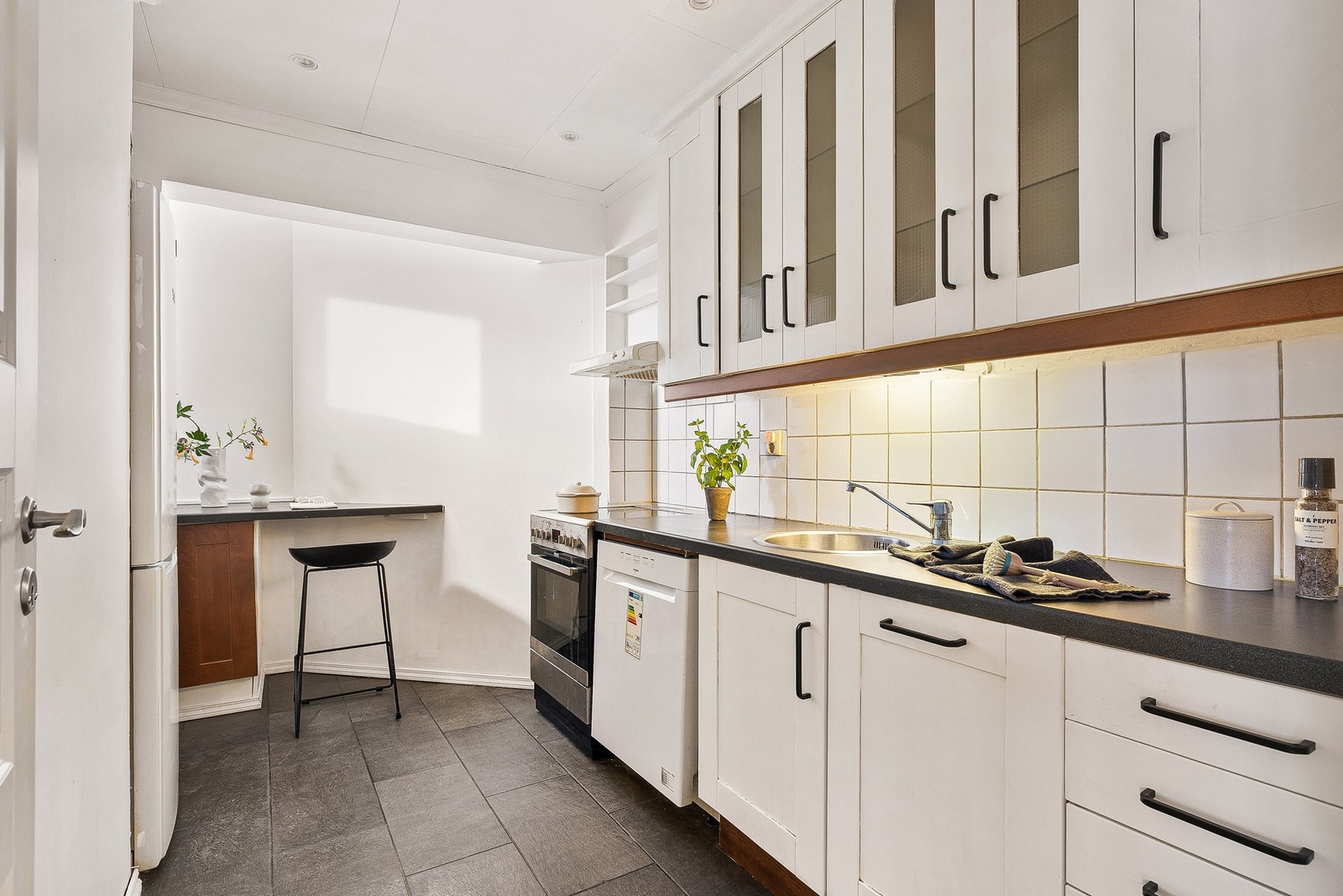 Kjøkkenet måler 7,5 kvm og har en tidløs innredning med profilerte fronter og laminat benkeplate med nedfelt stålvask. Galleribilde