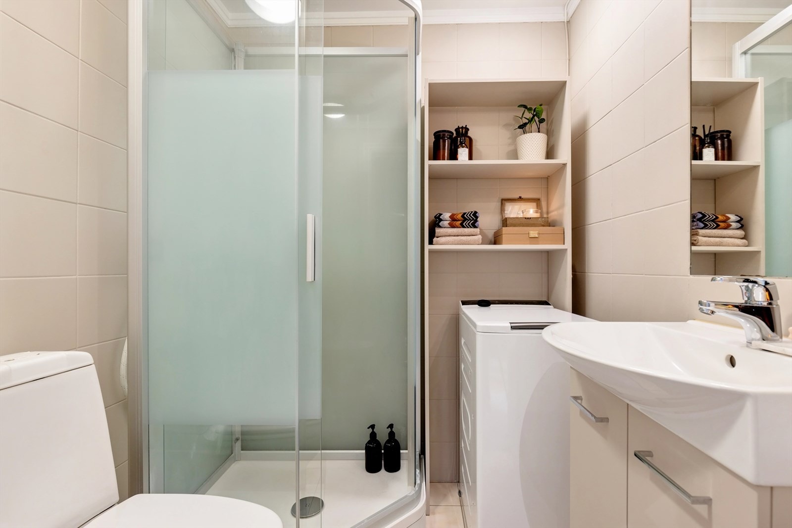 Flislagt bad med dusjkabinett, servant, toalett og opplegg for vaskemaskin. Galleribilde