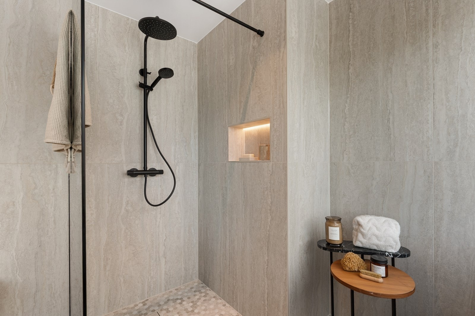 Dusjsone med glassvegg og integrert nisje med belysning. Store fliser og sorte detaljer gir et moderne og stilrent uttrykk. Galleribilde