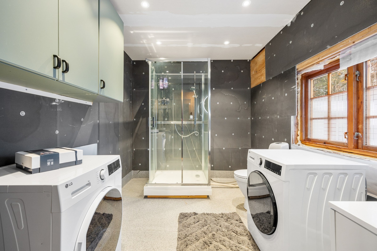 Badet har vegghengt servantinnredning med skuffer og ett-greps armatur, speil med overlys og stikk, vegghengt baderomsmøbel, dusjkabinett, gulvstående toalett og opplegg for vaskemaskin. Galleribilde