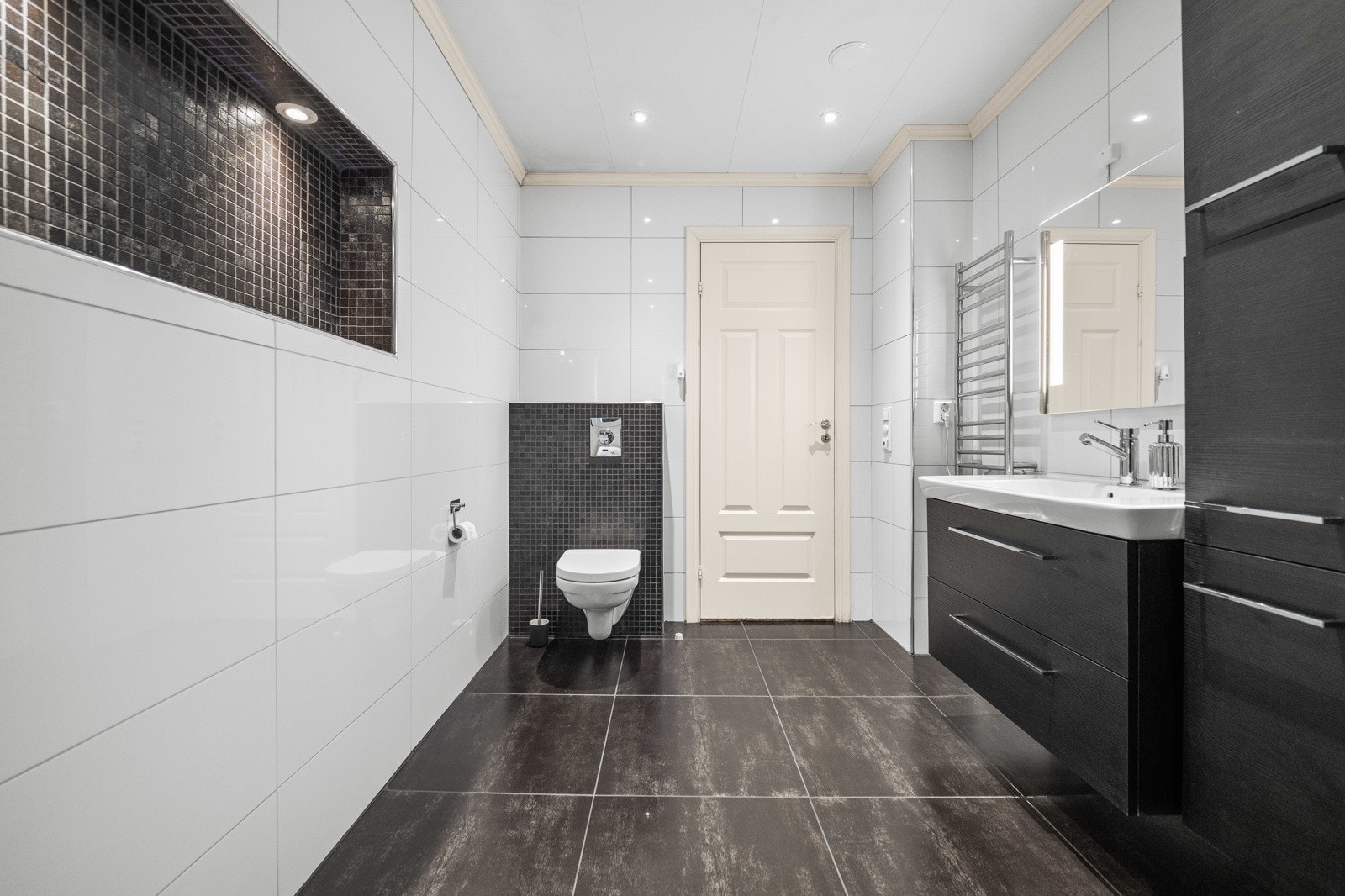 Badet består av innredning med oppbevaringsmuligheter, servant, dusjhjørne, elektrisk håndkletørker, samt vegghengt toalett Galleribilde