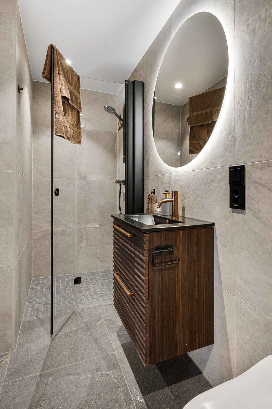 Badet har moderne innredning med nedfelt servant med skuffeseksjon, vegghengt toalett, speil og dusjhjørne med innfellbar glassdør og mosaikkfliser. Galleribilde