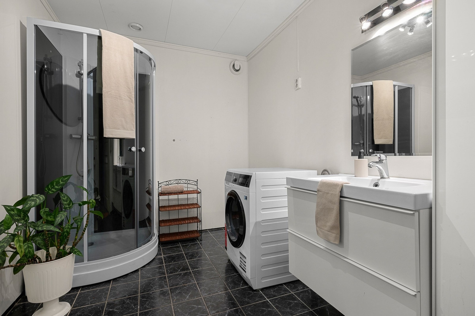 Tidløst bad med flislagt gulv og gulvvarme samt opplegg for vaskemaskin. Videre er badet innredet med dusjkabinett, toalett og servantskap med speil og lys. Galleribilde