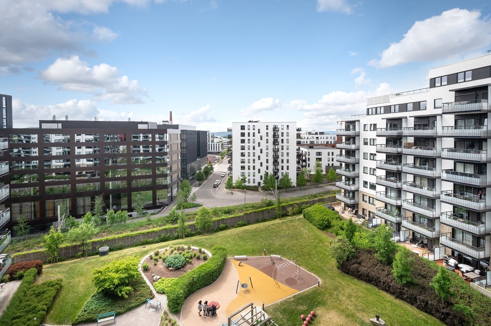 Utsyn over grønt og pent opparbeidet fellesareal med lekeplass og sosiale soner. Galleribilde