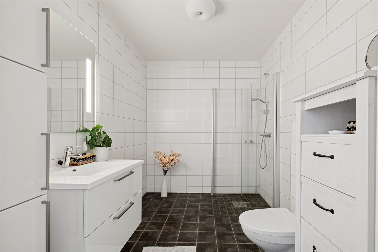 Badet er utstyrt med skap, servant med skuffer, speil med belysning og dusjhjørne. Balansert ventilasjon besørger for god utlufting. Galleribilde