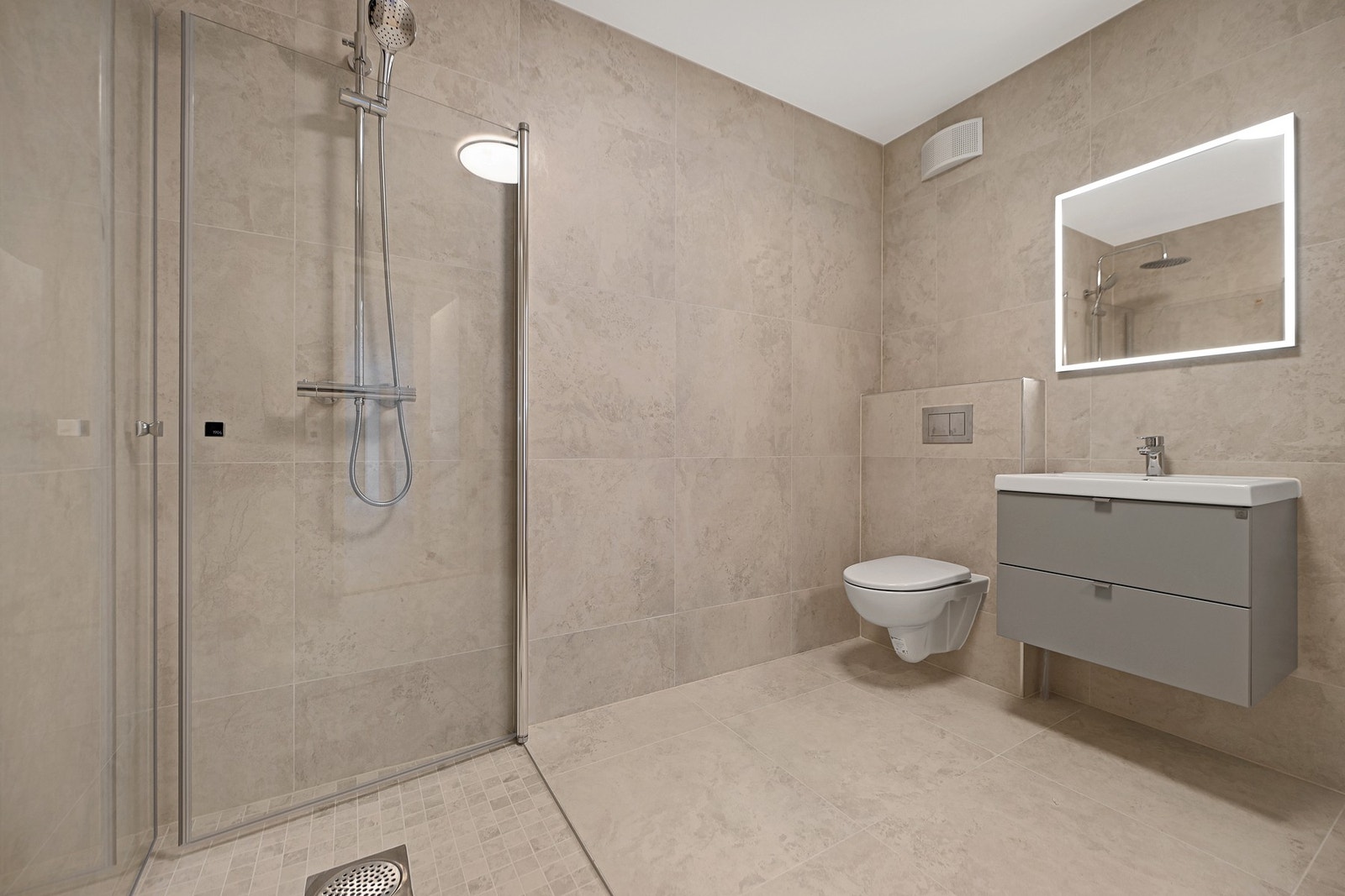 Badet er innredet med dusjhjørne med takdusj og hånddusj, vegghengt wc, servantskap, speil og opplegg for vaskemaskin. Galleribilde