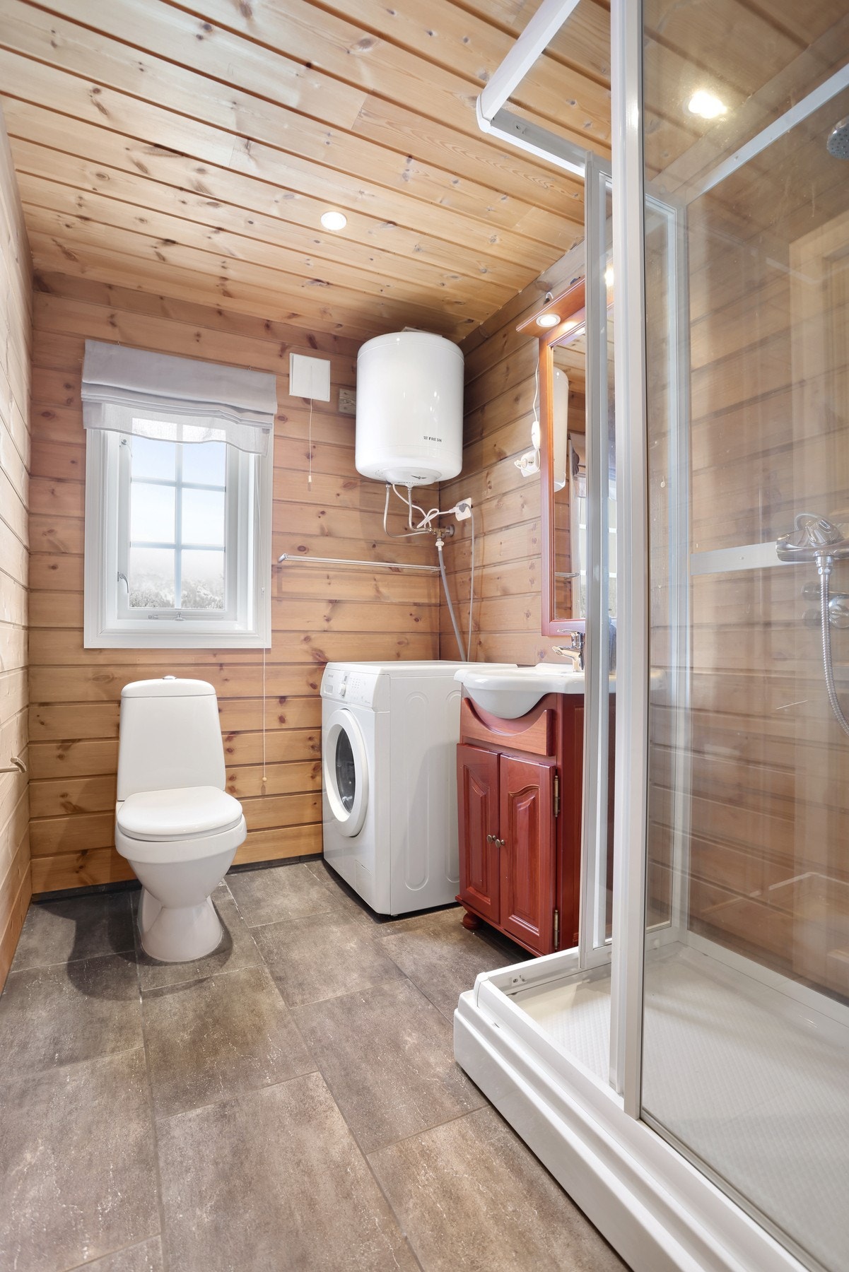 Bad II med flislagt gulv. Badet inneholder toalett, innredning med servant, dusjkabinett, opplegg til vaskemaskin og varmtvannstank Galleribilde