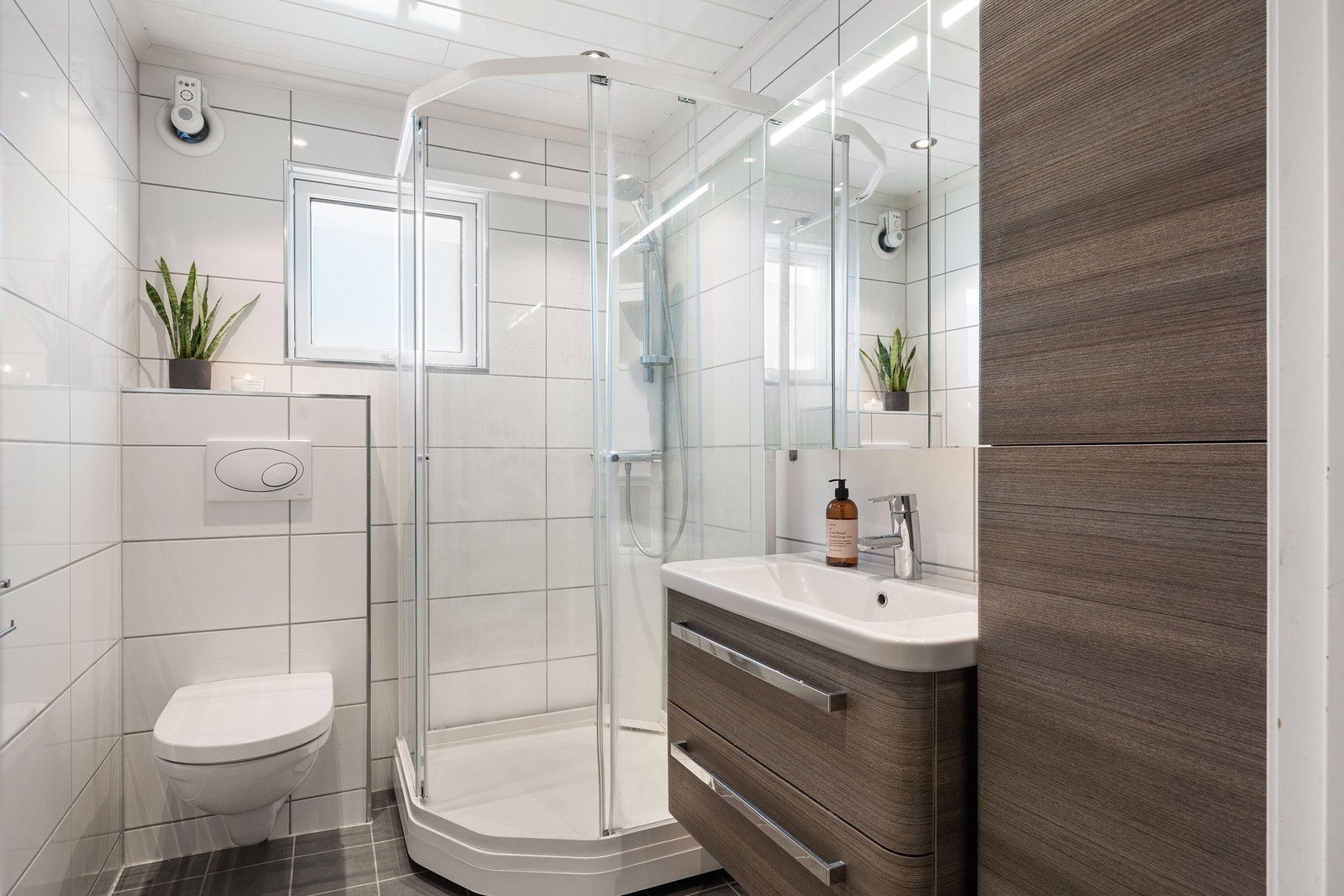 Badet er delikat innredet med dusjkabinett, vegghengt toalett og praktisk servantskap med speil. Galleribilde