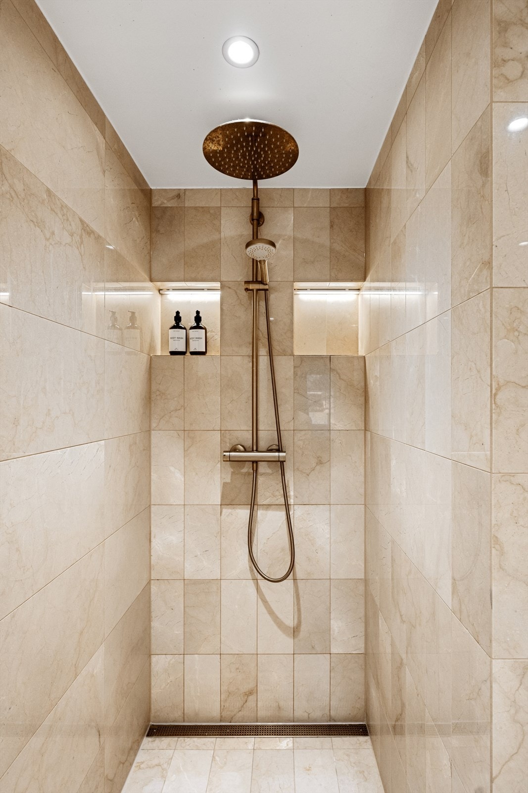 Regnfallsdusj i børstet messing i nisje med innebygde hyller med lyslist. Galleribilde