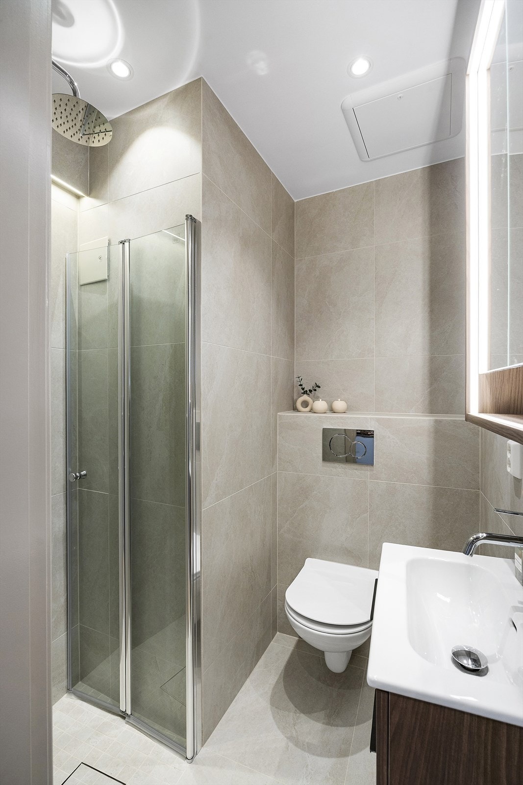 Veggfestet klosett med innebygget sisterne, dusjnisje med glassdør samt baderomsinnredning med speilskap og servant i helstøpt plate. Galleribilde