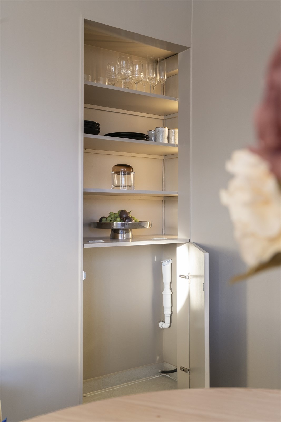 Delikat, åpen skapløsning med praktisk opplegg for vaskemaskin i skap, med gulvfliser og vannstopp-sensor. Galleribilde