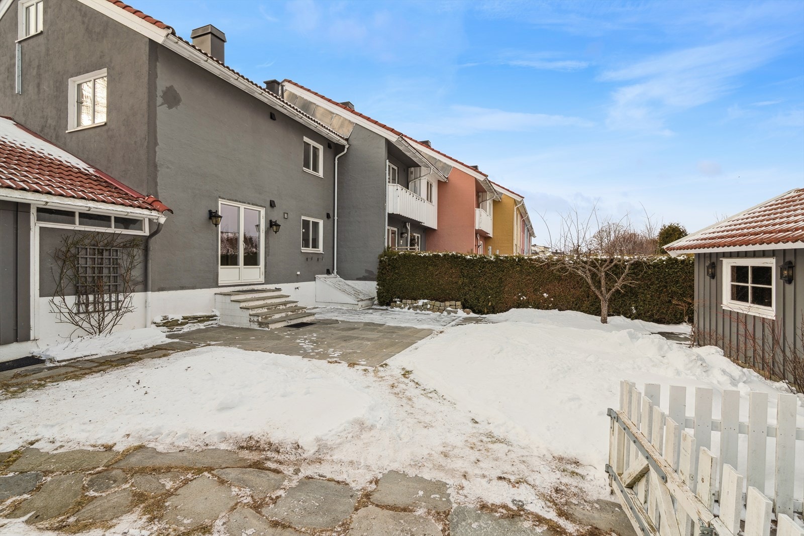 En flott og sjarmerende hage med vintergrønn tett hekk mot vei med hvit gjerde på utsiden av hekken. Tomten ligger som endetomt og har en av de største hagene i rekken. Galleribilde