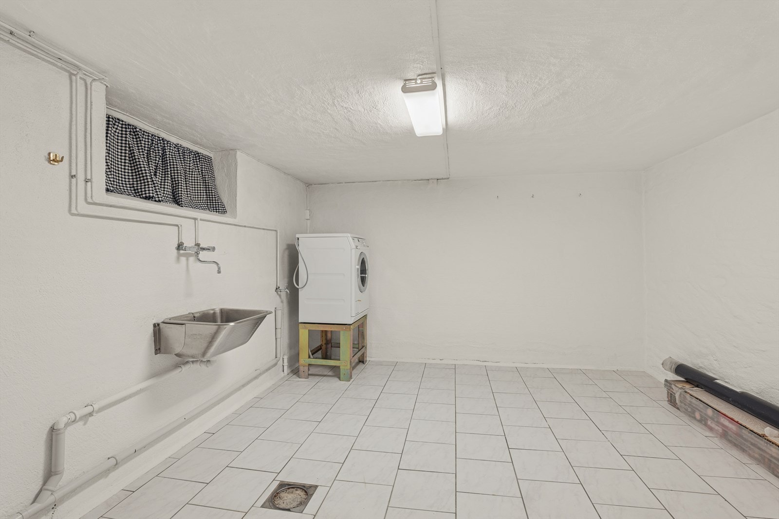 I denne etasjen ligger også et romslig vaskerom fra byggeåret, utstyrt med støpt gulv belagt med fliser og behagelige varmekabler. De malte murveggene gir et robust og praktisk preg, og rommet har både skyllekum og opplegg for vaskemaskin. Galleribilde