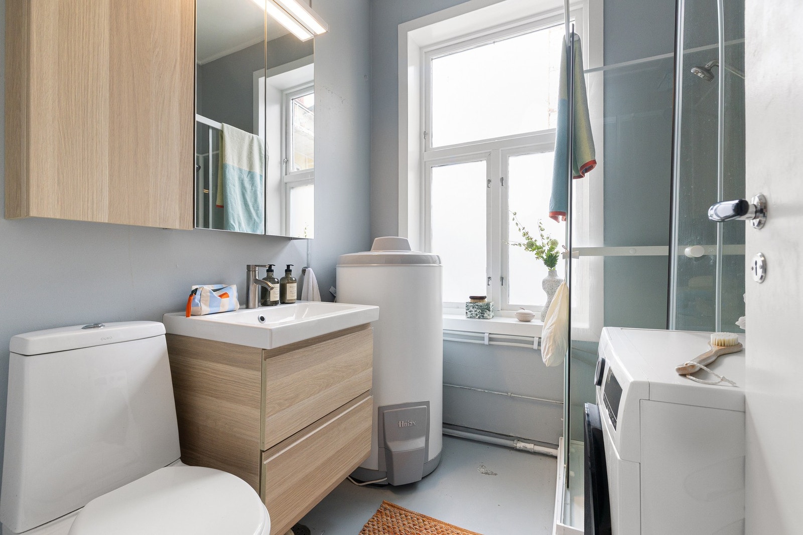 Badet er praktisk innredet med dusjkabinett, servant med skuffeseksjon, toalett og opplegg for vaskemaskin Galleribilde