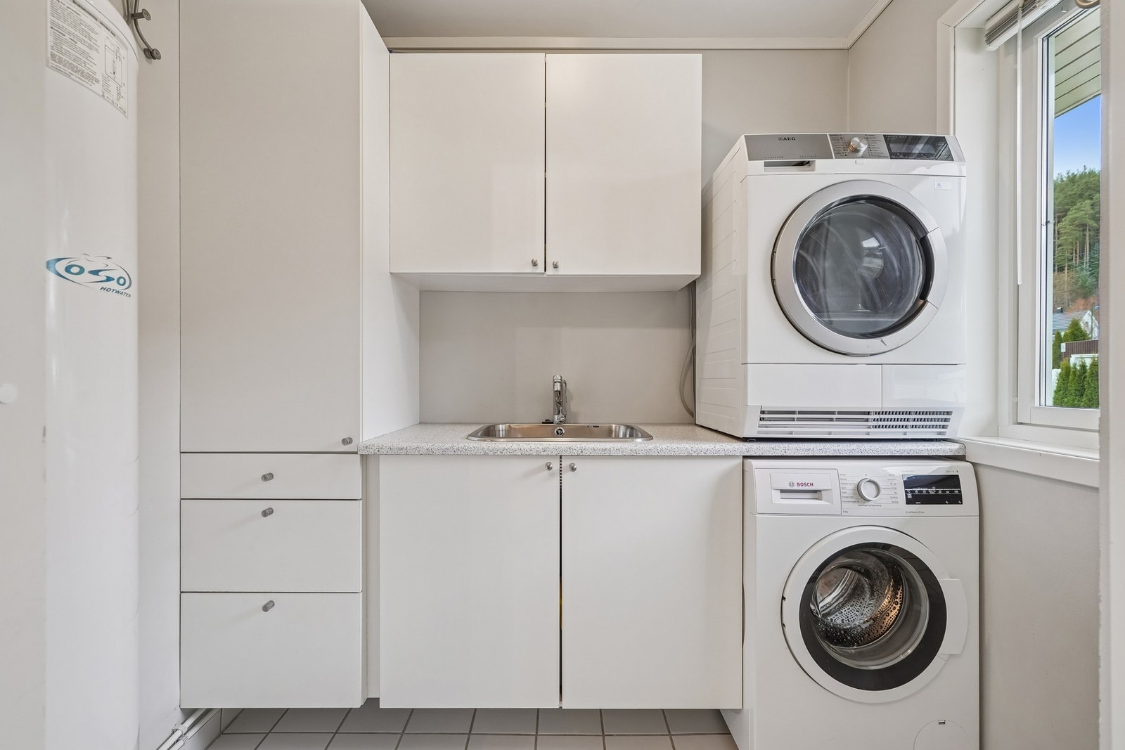 Vaskerom med fliset gulv med varmekabler i. Flott og praktisk innredning med utslagsvask og opplegg for vaskemaskin og tørketrommel. Galleribilde