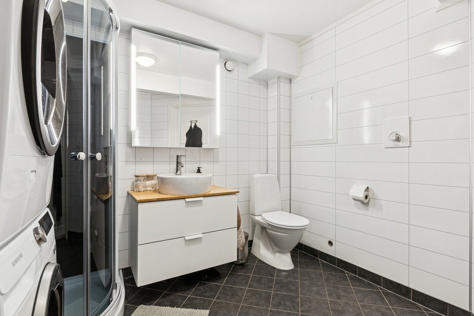 Badet er innredet med toalett, dusjkabinett og baderomsinnredning med to skuffer, toppservant, speilskap med integrert lys, høyskap og opplegg for vaskemaskin. Galleribilde