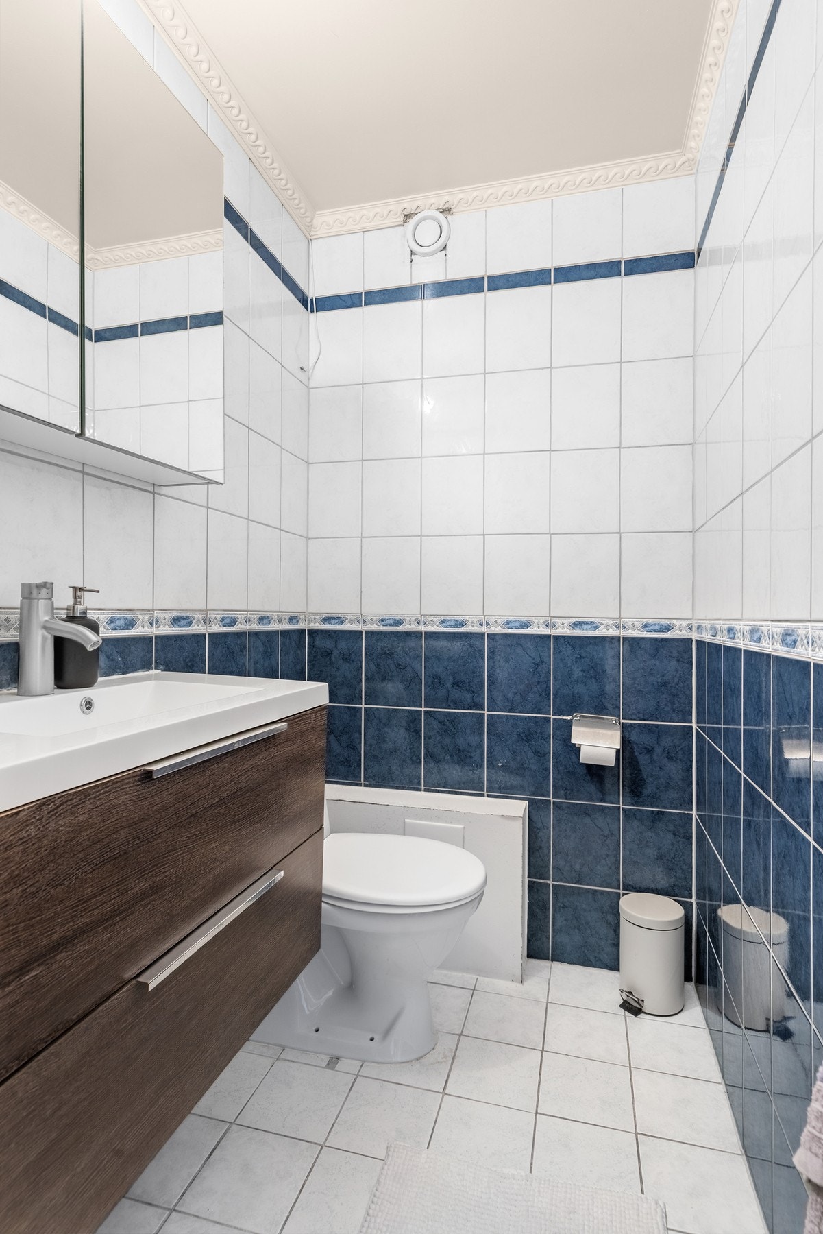 Flislagt toalettrom med gulvmontert toalett og moderne servantseksjon med skuffer. Speil over servant og naturlig ventilasjon gir et lyst og funksjonelt rom. Galleribilde