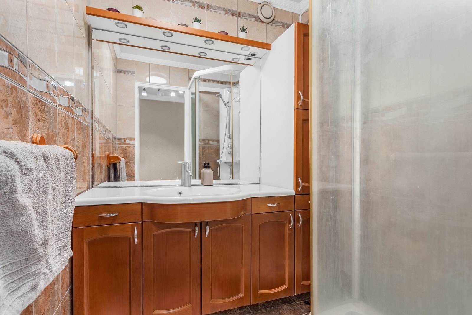 Romslig og funksjonelt bad med flislagte overflater og behagelig varme i gulvet. Servantseksjon med god oppbevaringsplass og speil over benk gir et praktisk og ryddig uttrykk. Galleribilde