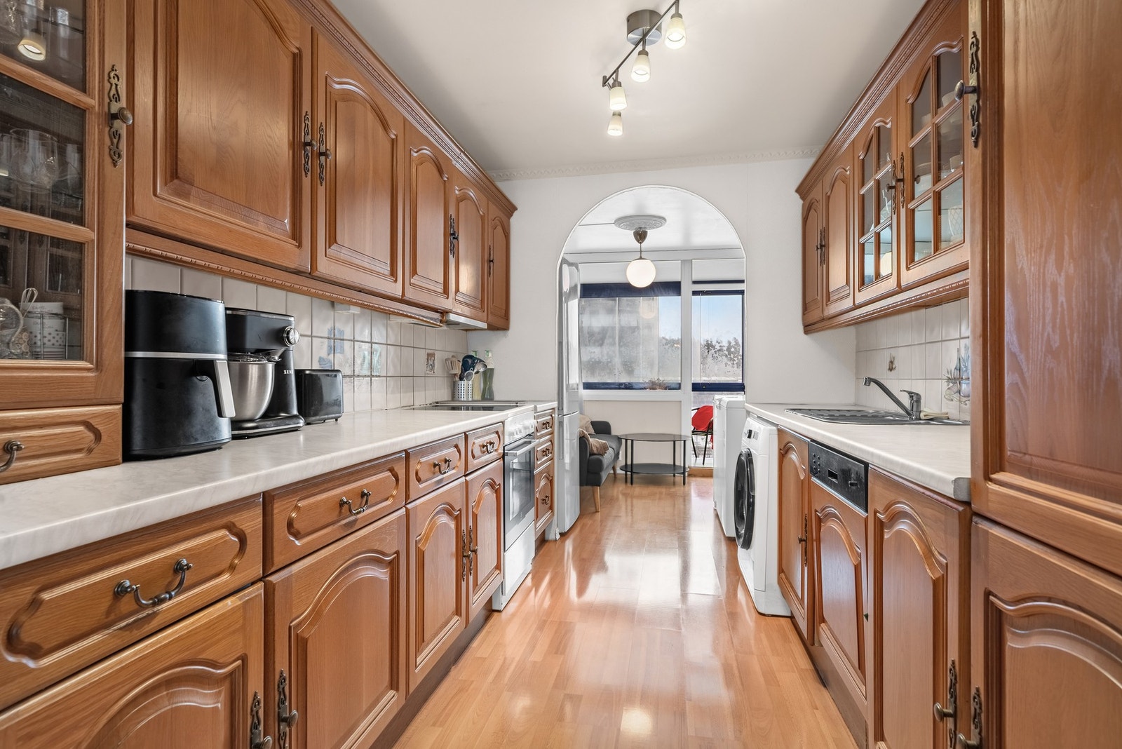 Kjøkken med profilerte fronter, laminat benkeplate og fliser over benk. Nisjer for hvitevarer og ventilator over kokesone. Galleribilde