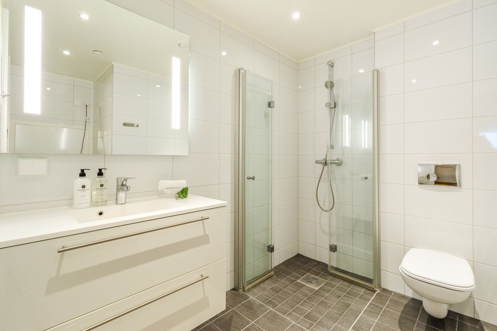 Lyst og delikat baderom med dusjhjørne, toalett og opplegg vaskemaskin. Leiligheten har også ekstra gjestetoalettrom i tillegg til det som er på baderommet. Galleribilde