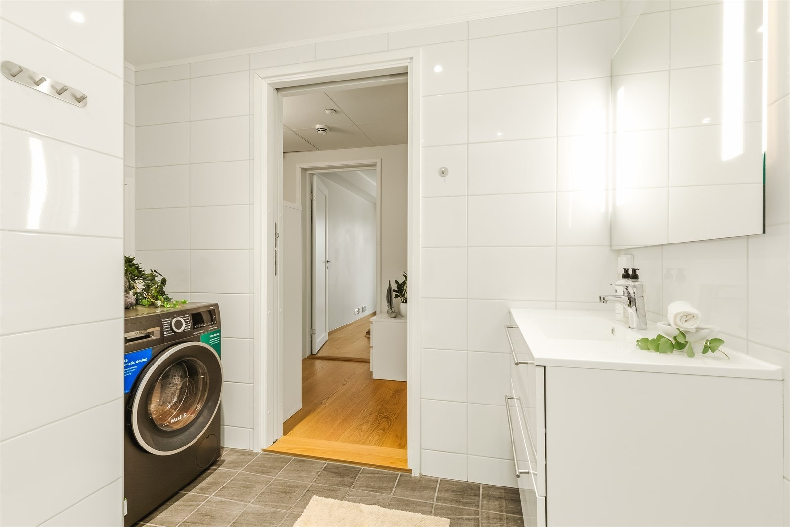 Baderomsinnredning hvor servantskap har fronter i hvit utførelse fra Arens med to brede kolonialskuffer med god oppbevaringsplass. Det er også vegghengt toalett. Opplegg til vaskemaskin og tørketrommel hvor plass til dette er i inntrukket nisje. Galleribilde