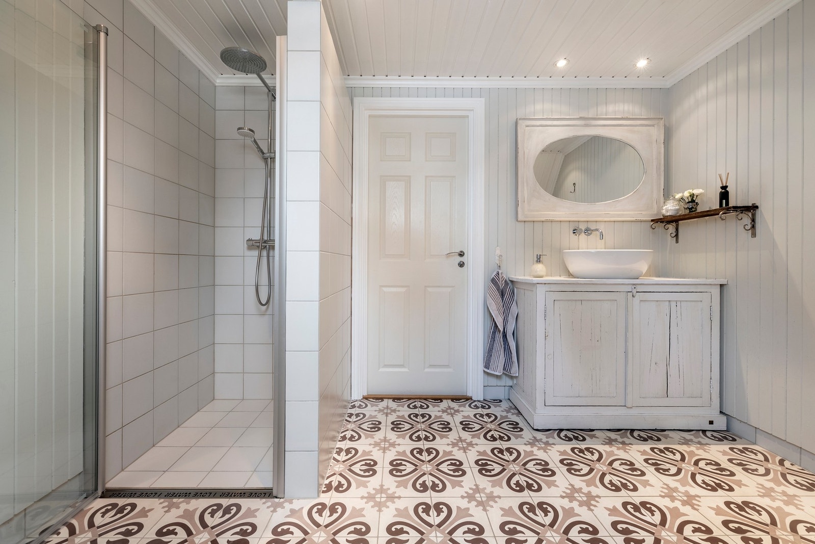 Badet har downlights, flislagt gulv og vegger med trepanel, kombinert med fliser i dusjsonen. Galleribilde