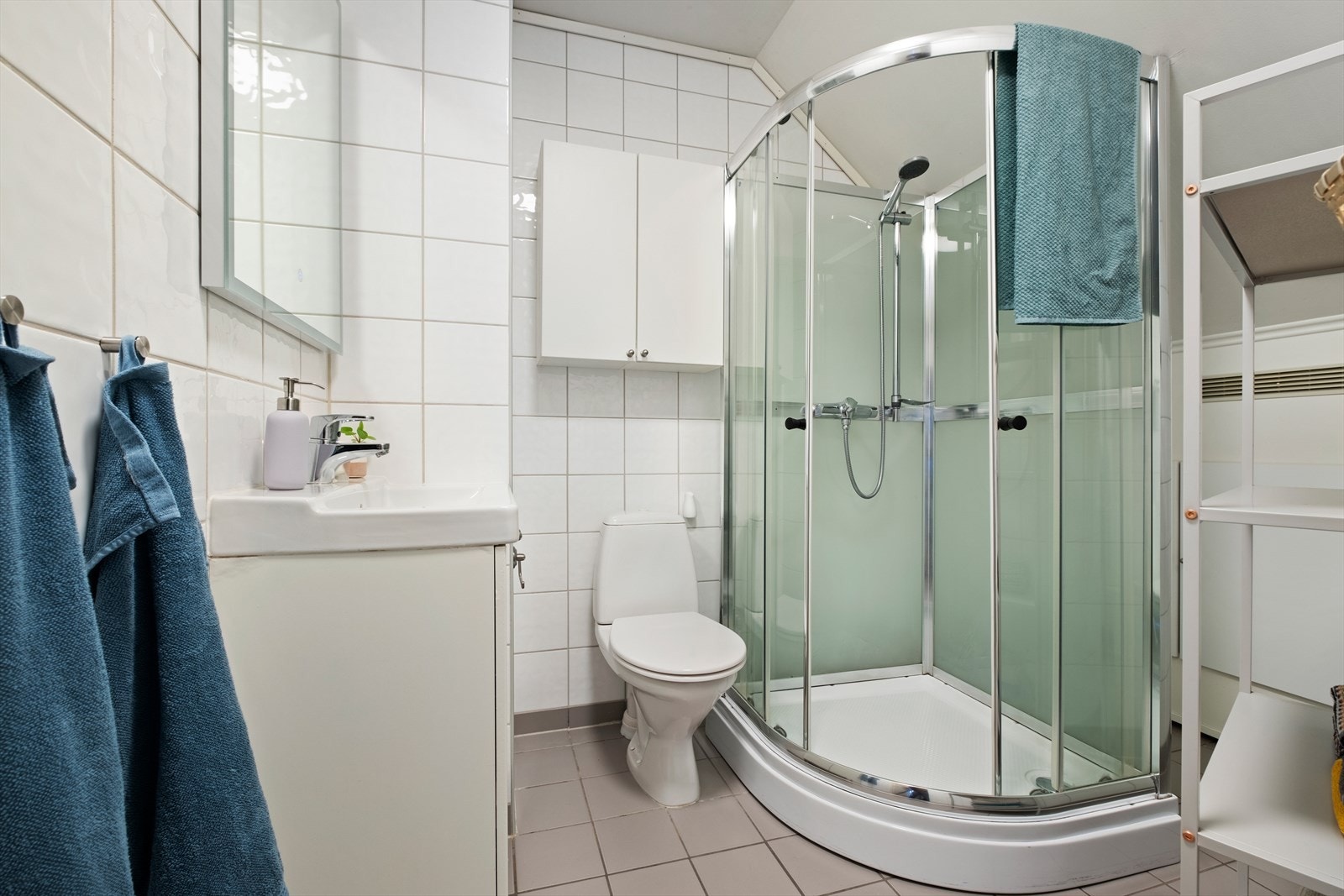 Badet er 4,5m² med flislagt gulv og vegger. Det er innredet med dusjkabinett, toalett, innredning med servant og opplegg for vaskemaskin. Galleribilde
