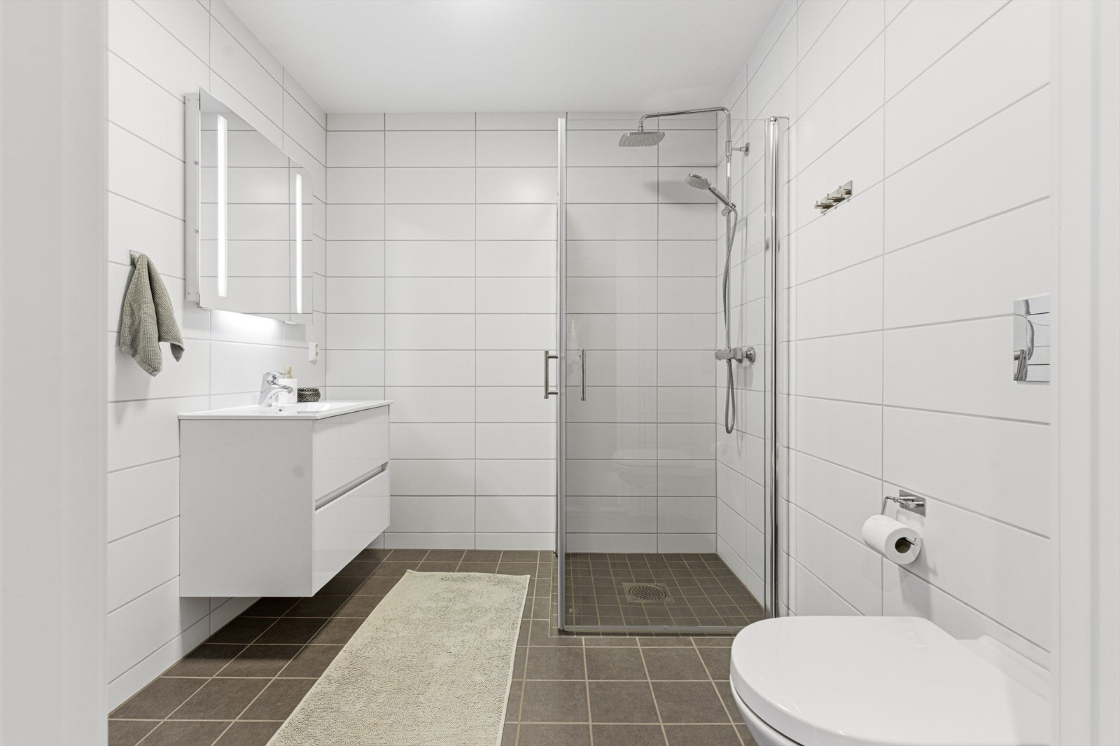 Det første badet ligger i boligens 1. etasje. Her er det grå tidløse fliser på gulv og hvite fliser på veggene. Galleribilde