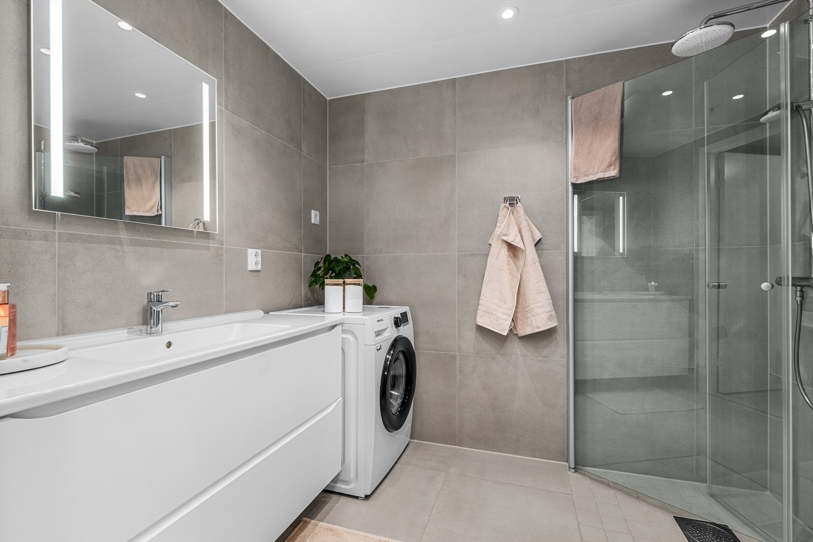 Lekkert flislagt bad med behagelig gulvvarme. Her får du veggfestet innredet servant, opplegg for vaskemaskin og praktiske innfellbare dusjdører. Galleribilde