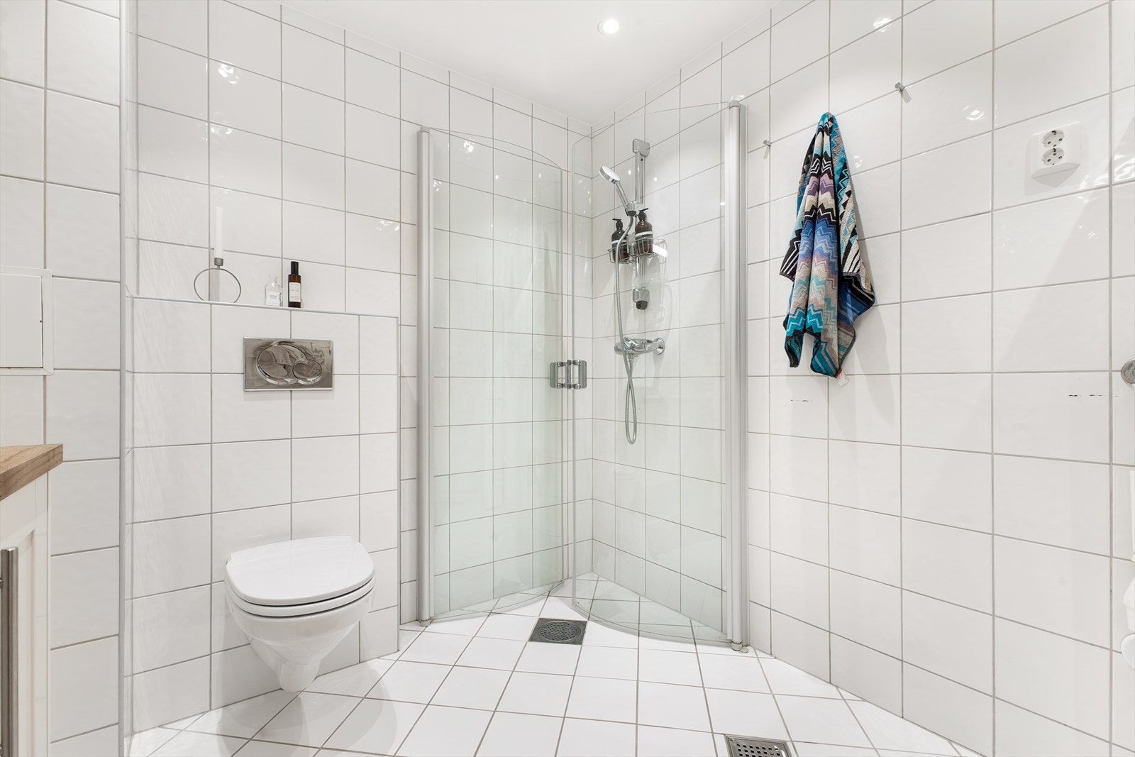 Badet har dusjhjørne med plassbesparende glassdører og veggmontert toalett, samt varmekabler i gulvet. Galleribilde