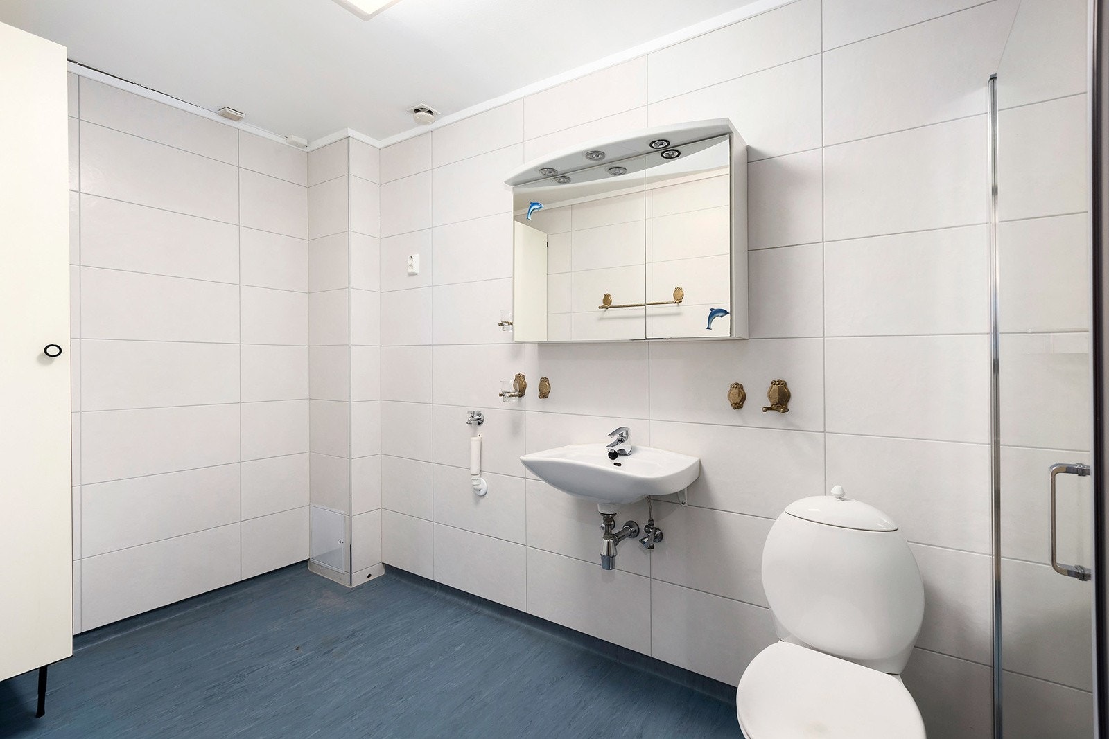 Innredning med vegghengt servant, veggskap med speilfronter og belysning, gulvmontert toalett, dusjvegger/hjørne og opplegg for vaskemaskin. Galleribilde