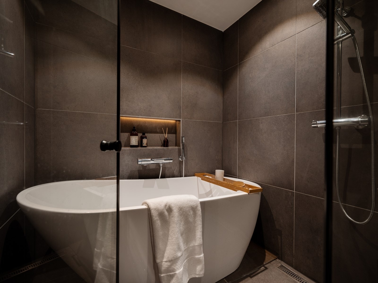 En integrert nisje i flisveggen gir en stilren oppbevaringsløsning ved badekaret. Galleribilde