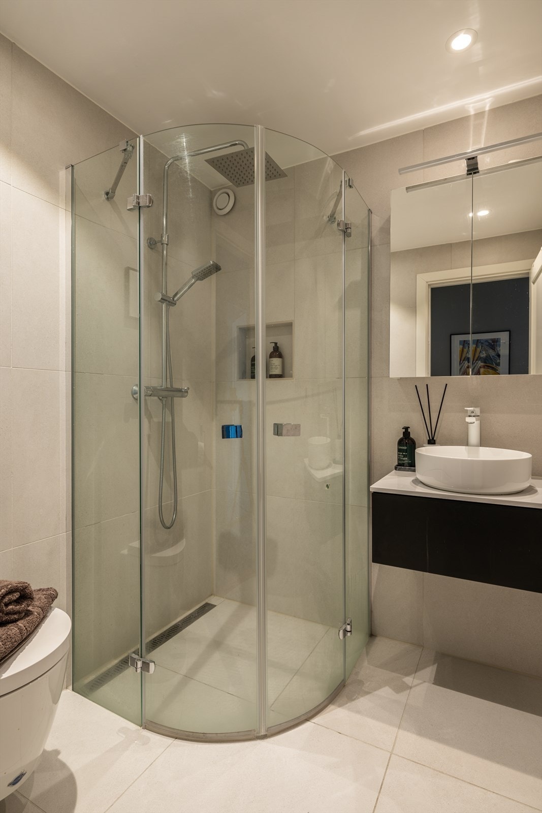 Badet er innredet med dusjhjørne med svingbare glassdører og speilskap med lys. Galleribilde