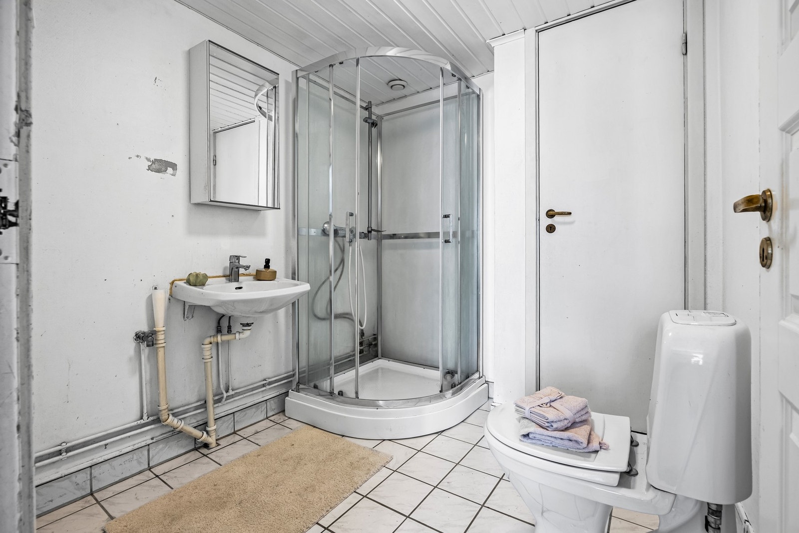 Badet har flislagt gulv med varmekabler og er innredet med dusjkabinett, veggmontert servant og gulvstående toalett, i tillegg til opplegg for vaskemaskin. Galleribilde