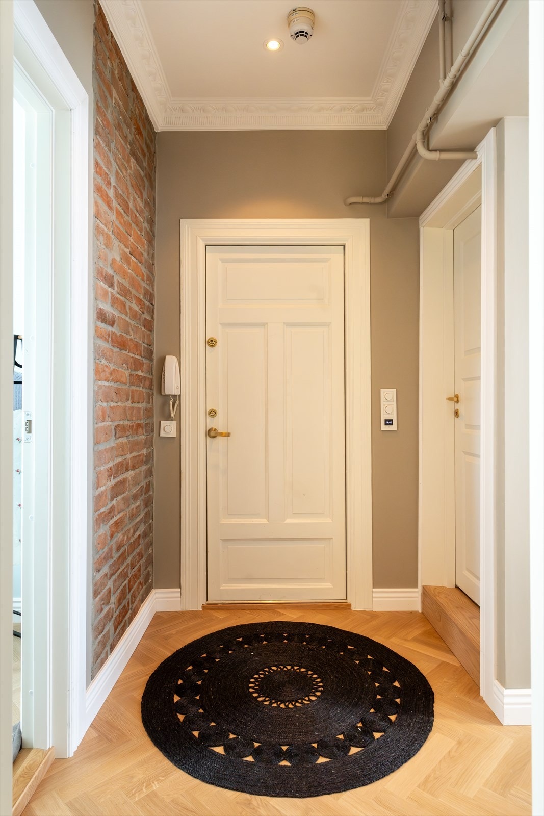 Entréen har god takhøyde, delvis eksponert teglsteinsvegg, stukkatur og lekker en-stavs fiskebensparkett. Galleribilde