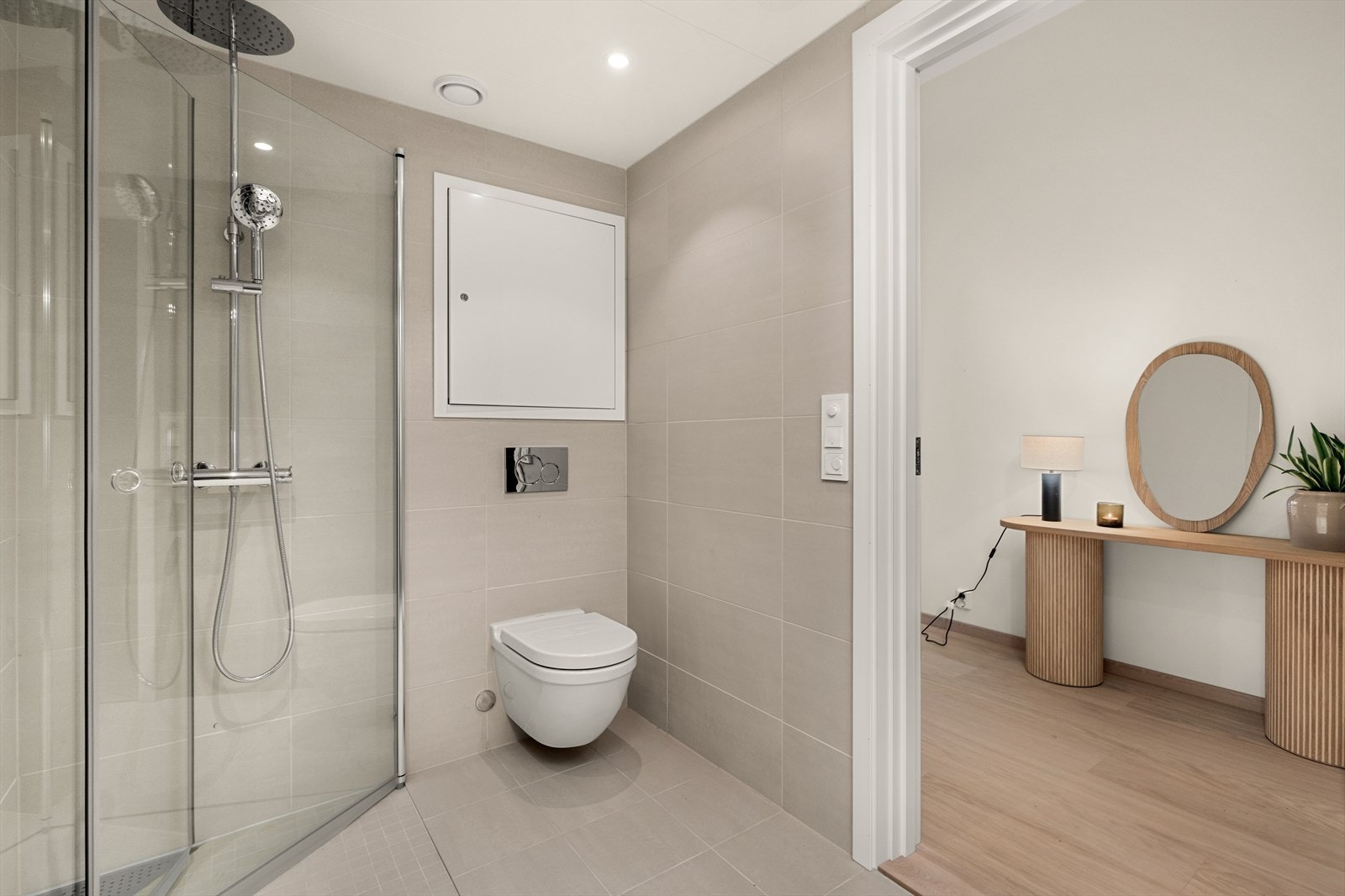 Her får du et lekkert flislagt bad som er innredet med åpen dusjløsning med praktiske innfellbare glassdører, baderomsinnredning med speilskap og
servant, opplegg for vaskemaskin, veggmontert wc og downlights Galleribilde