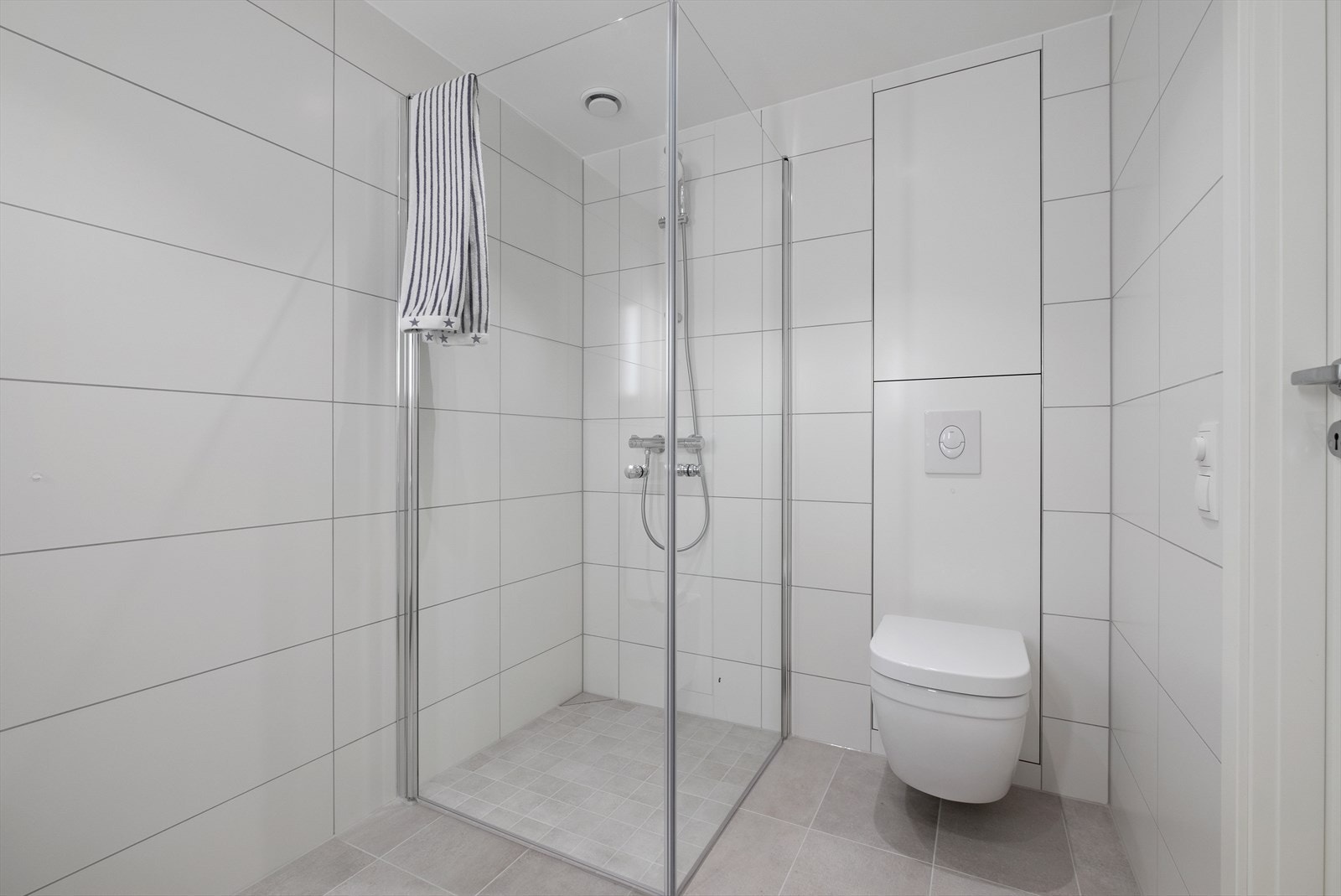 Badet er innredet med praktiske innfellbare dusjdører, opplegg for vaskemaskin, veggmontert WC- og innredet servant. Galleribilde
