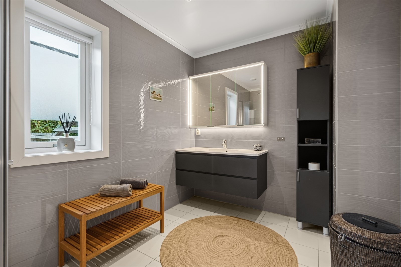 Badet er helfliset og innredet med en praktisk og stilfull innredning med god oppbevaringsplass og frittstående høyskap, nedfelt servant og vegghengt speilskap. Galleribilde