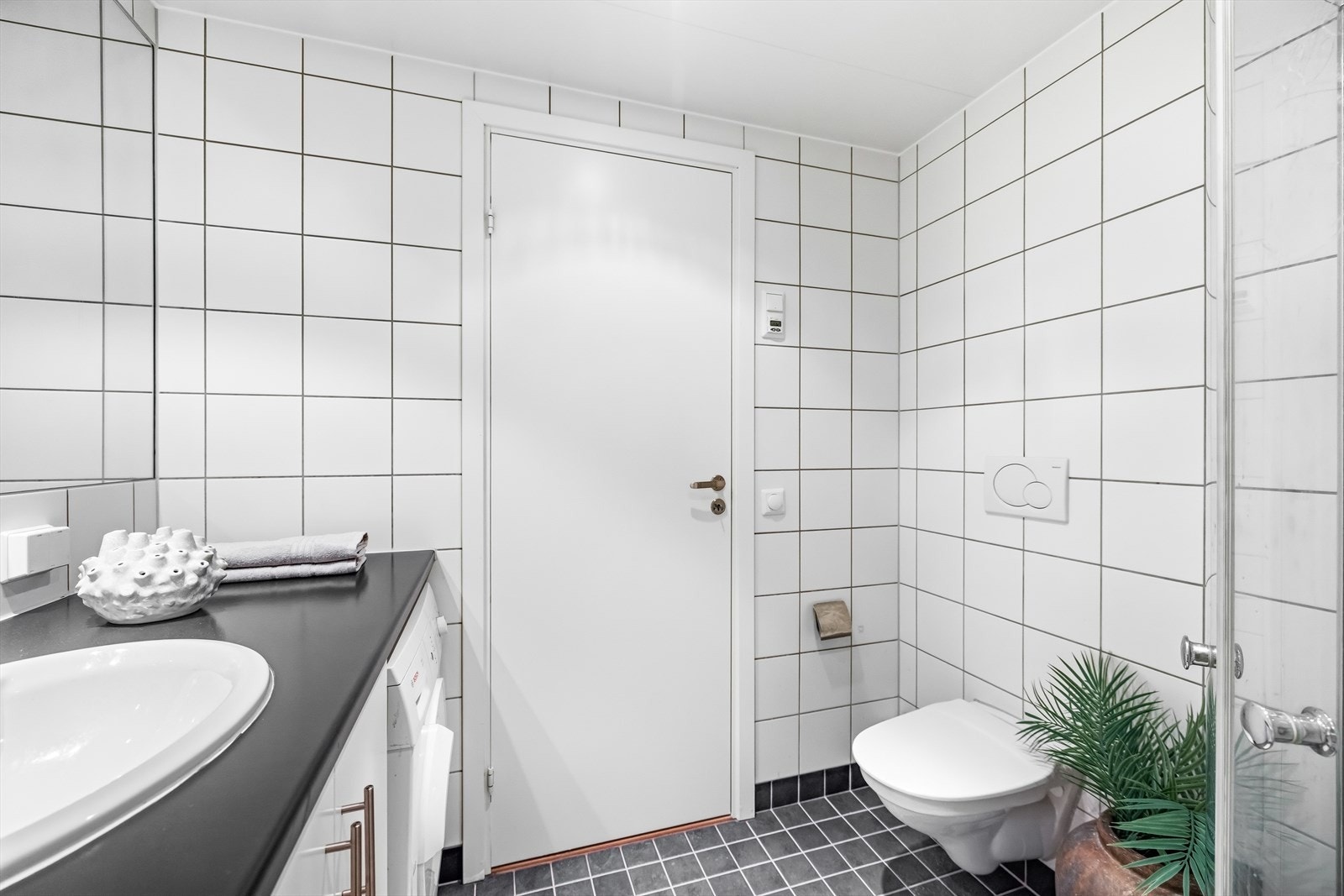 Badet er utstyrt med vegghengt toalett, servant med underskap, speil, samt dusjhjørne med innfellbare glassdører - en plassbesparende og stilren løsning Galleribilde