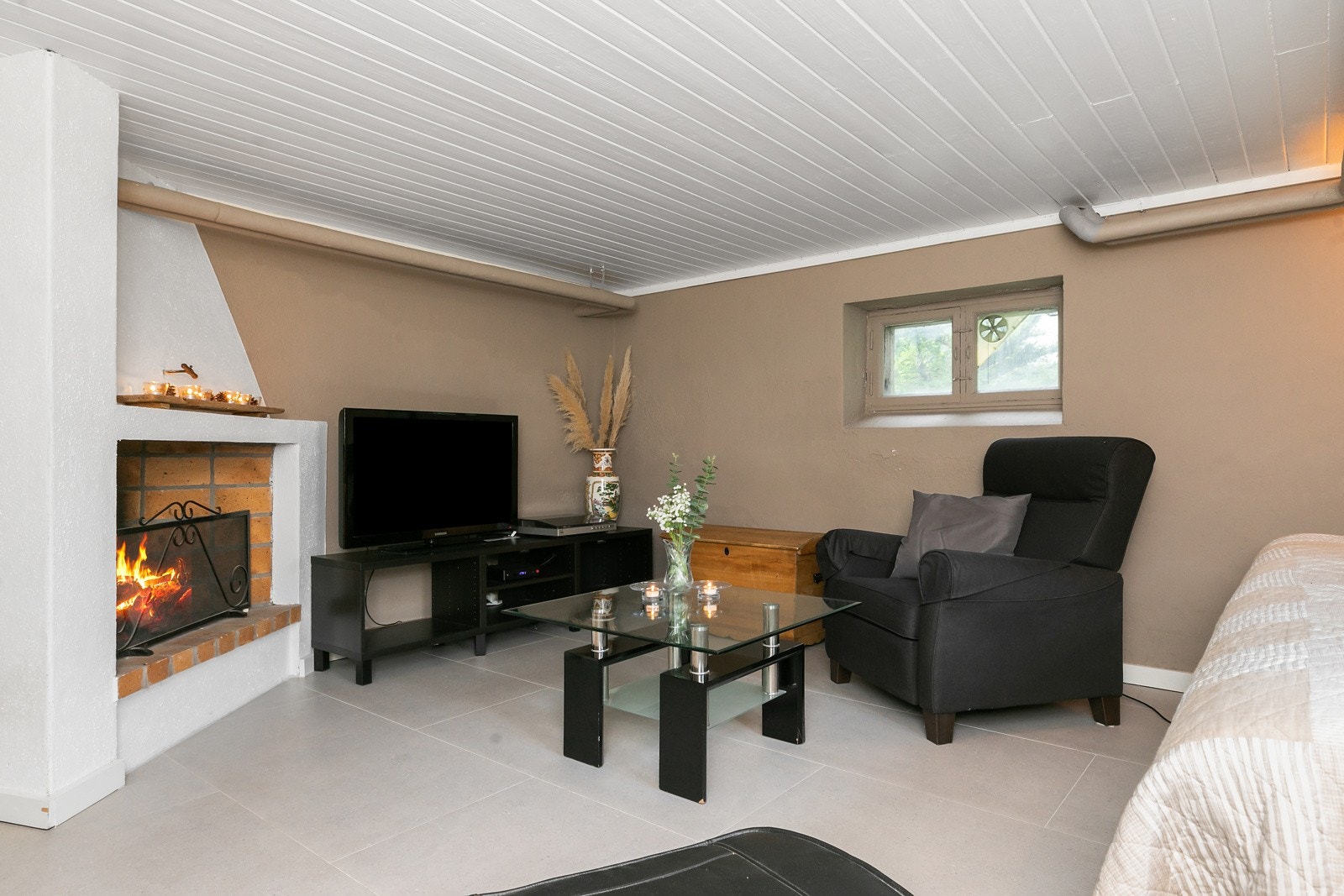 Kjellerstue med peis, vannbåren varme og fliser på gulv. Galleribilde