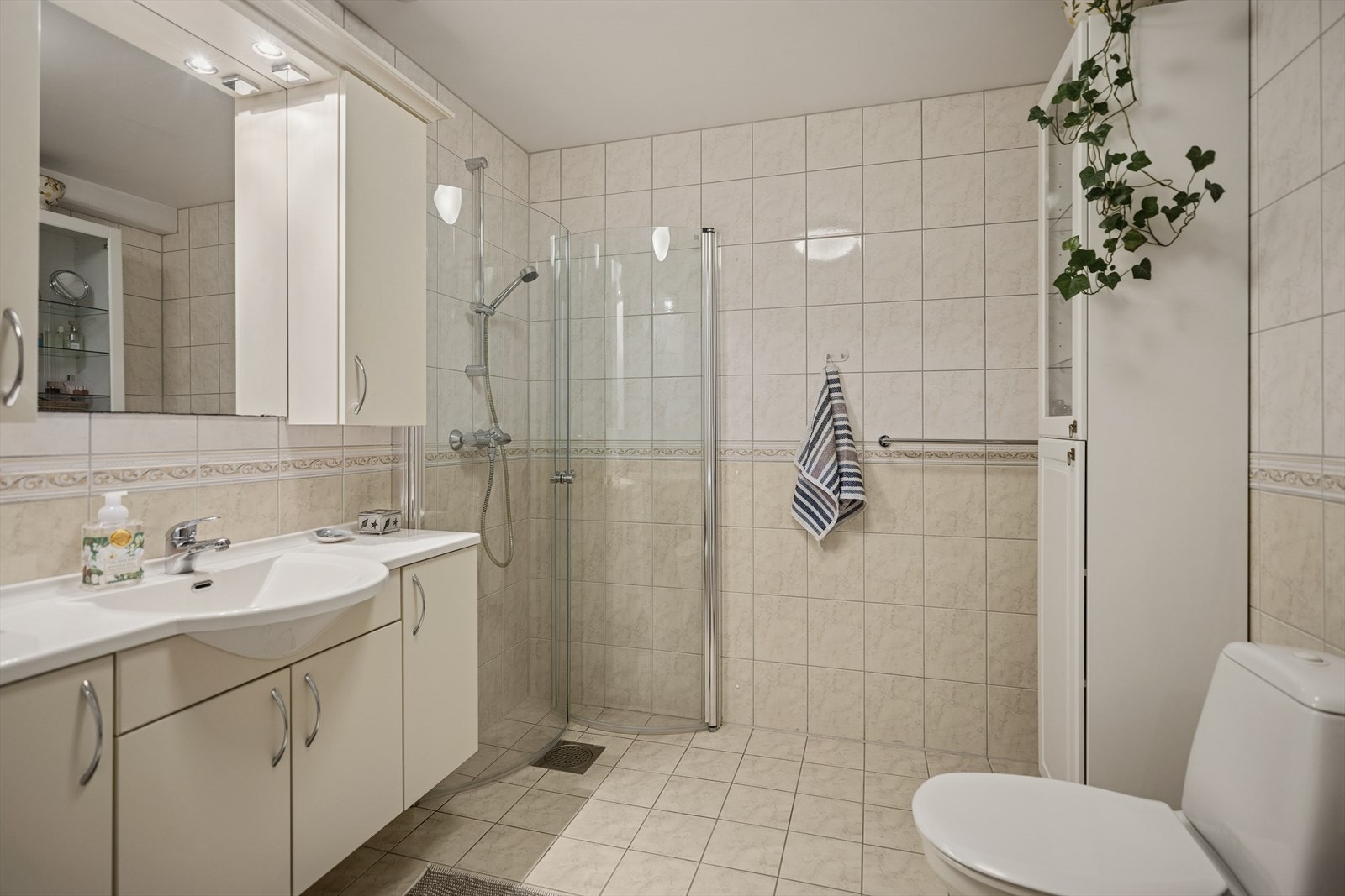 Baderommet har et stor baderomsmøbel med speil og overskap, gulvstående toalett og innfellbart dusjhjørne Galleribilde